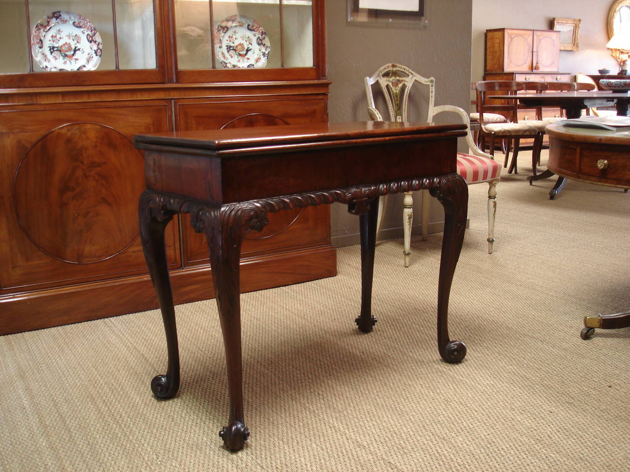 George II period mahogany cabriole leg card table, in the manner of Thomas Chippendale. The top with gadrooned trim, centred with leaf motif and the legs with low relief acanthus, swag and rosette carving, terminating in French scroll feet,