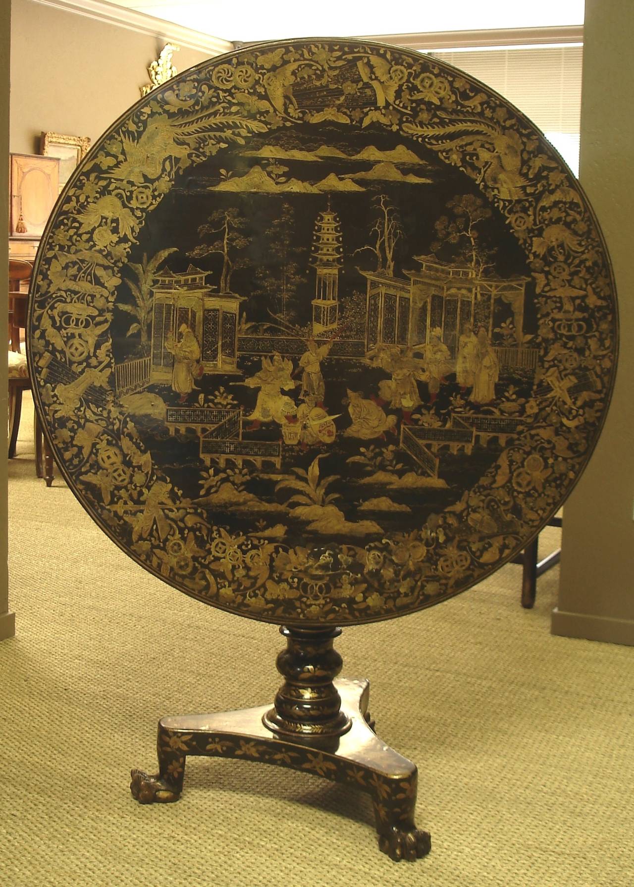 Chinese export lacquer and gilt decorated tilt-top table. The circular top decorated with figures engaged in courtly activities within a foliate border. The top above a birdcage action, with gilt decorated pedestal and tripod legs with ball and claw