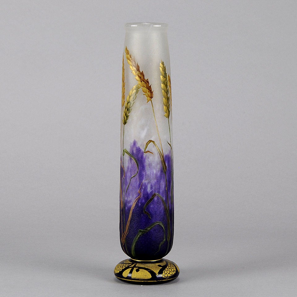 A French Art Nouveau glass vase celebrating fertility and the harvest by Daum. The vase features multi-hued wheat stalks swaying against a graduated purple and white ground and suspended above acid etched and enamel gilt decoration around the base. 
