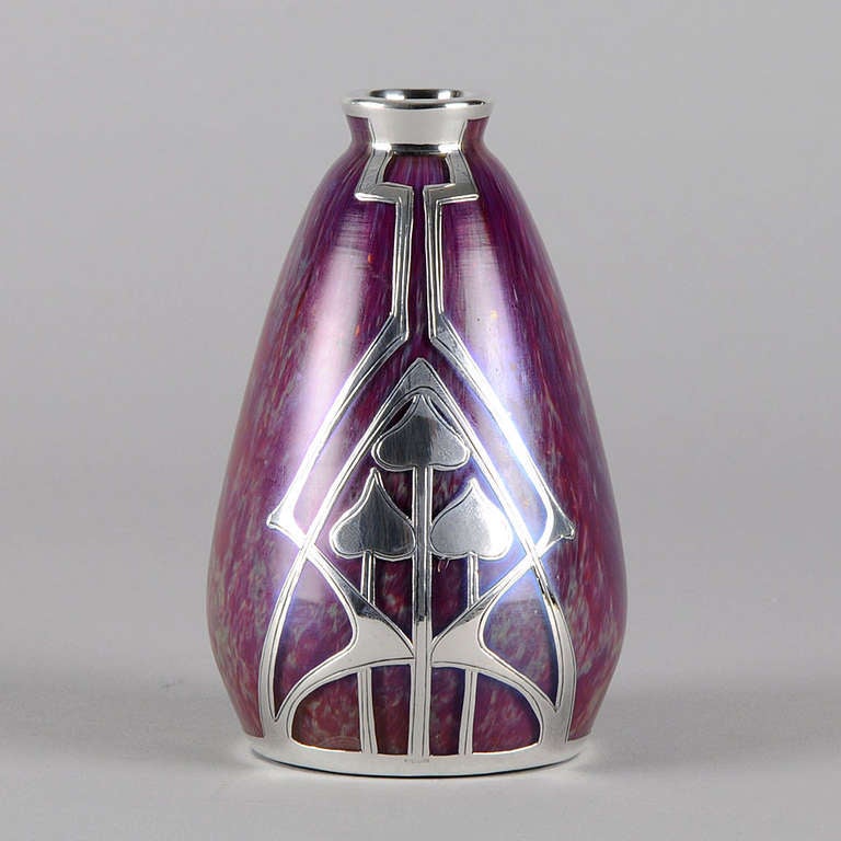 A stunning early 20th Century Art Glass vase of eye catching Raspberry glass with beautiful irridescent overlay, enhanced with a stricking geometric silver overlay. 