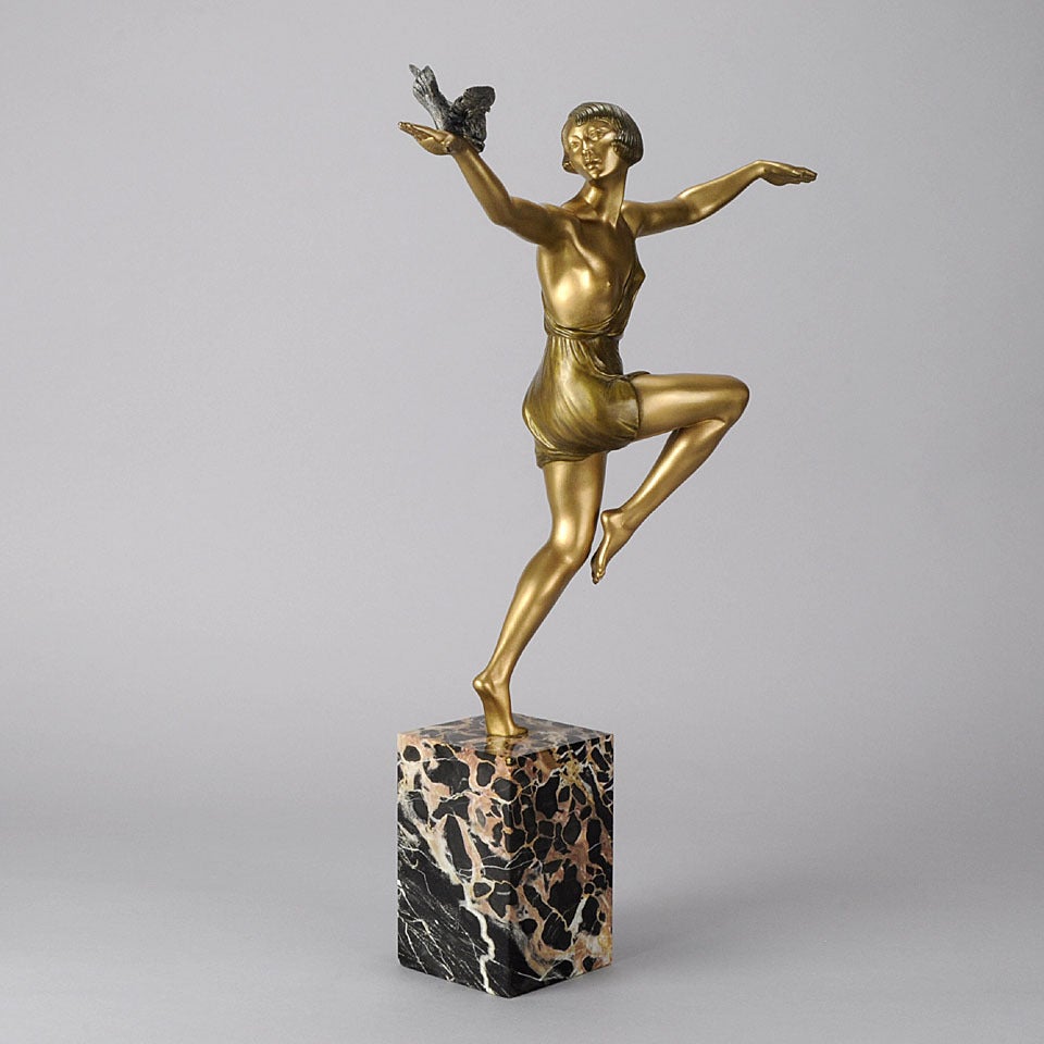 An elegant French early 20th Century cold painted bronze figure of a beautiful Art Deco dancer in a striking stylised pose holding a bird in her hand with excellent rich golden colour and fine hand finished detail, signed Faguays on top of square