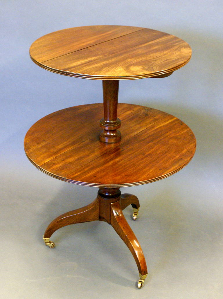 In finely grained Cuban mahogany, standing on original square cup castors, the tripod base supporting a turned column which in turn supports the two folding tiers that are finished on the edge with a triple reed. This piece is in good original