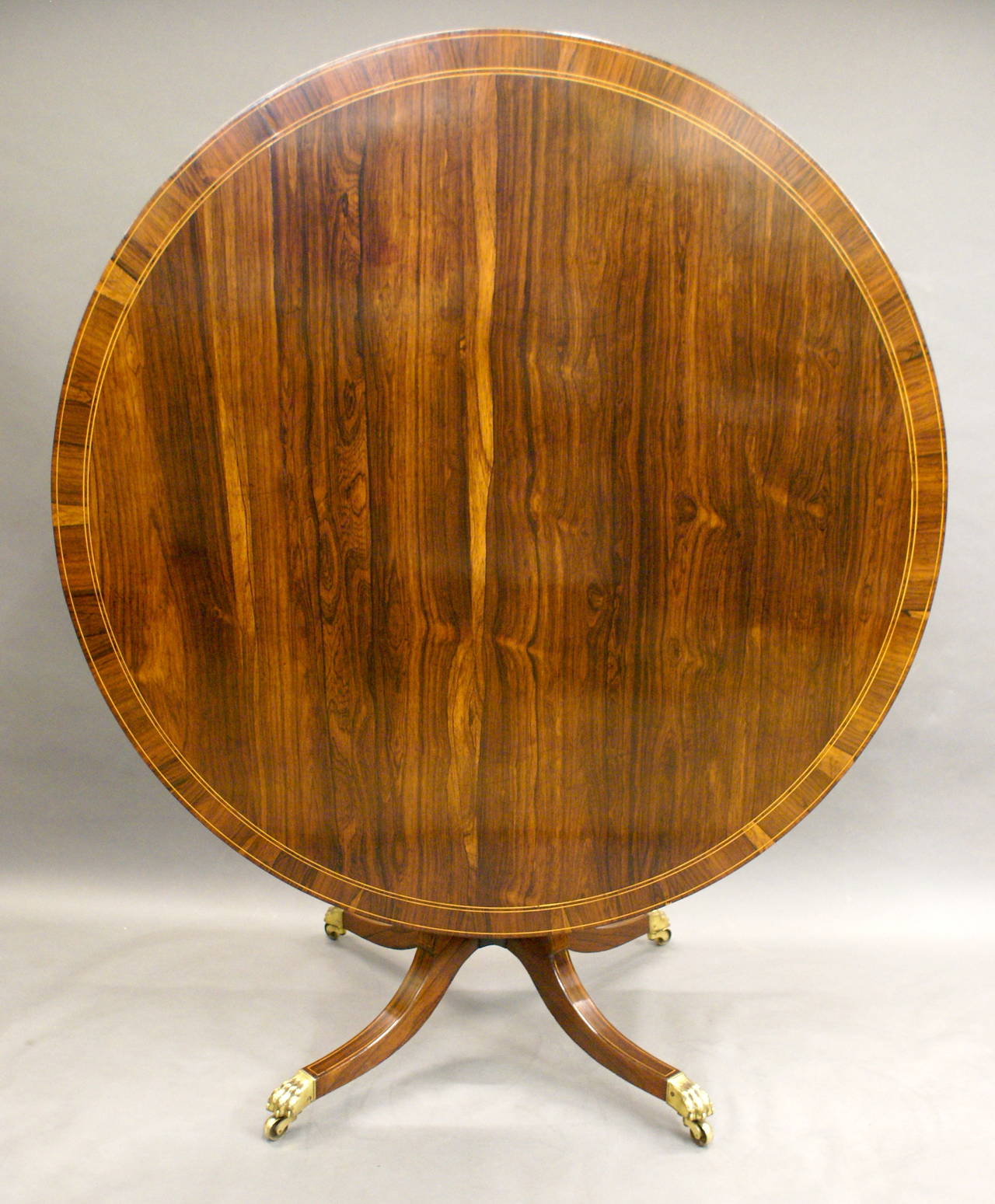 This table is in Rio rosewood that has faded to a beautiful mellow colour. The base has a turned baluster column and 4 boxwood strung legs that terminate in the original gilt brass castors. The top is banded and boxwood strung and retains its