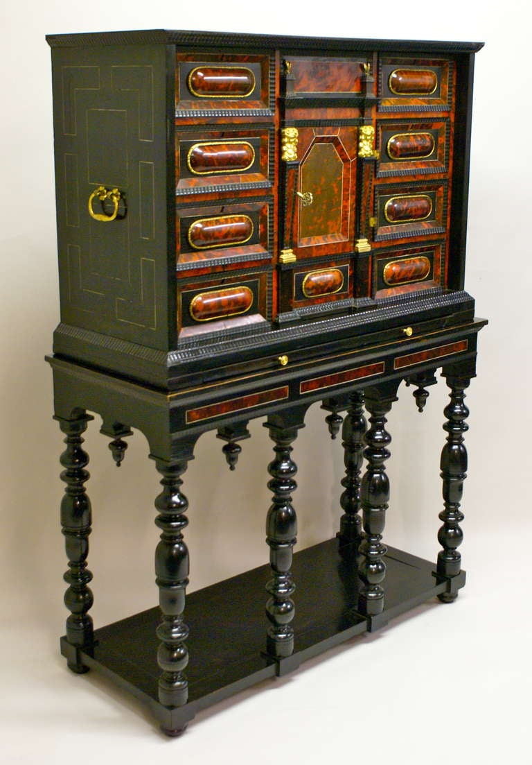 An Antwerp ebonised and red-stained tortoiseshell cabinet, the moulded cornice above a panelled drawer and door enclosing a fitted, perspectived interior with a mirrored colonnade and chequered floor, and flanked by four cabochon-moulded drawers