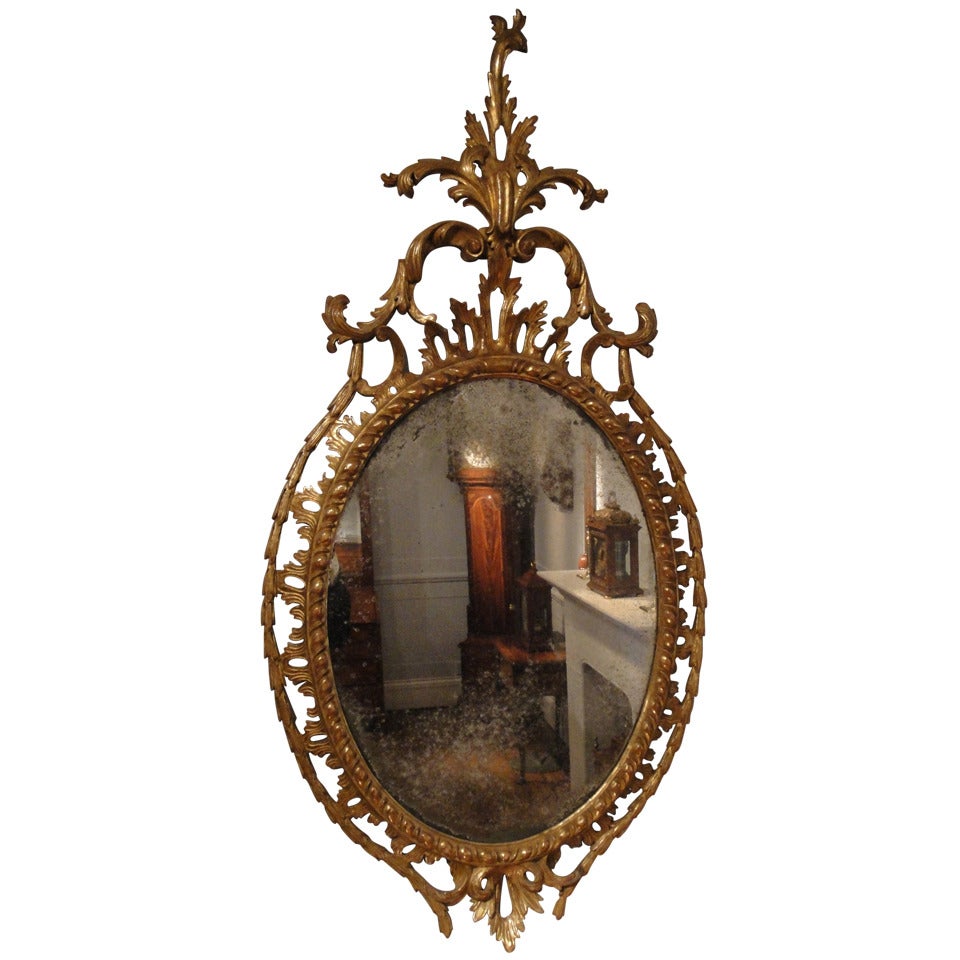 A fine and most attractive antique Chippendale period carved wood and gilt oval mirror, topped with an elaborate Rococo cartouche cresting consisting of acanthus leaves and C-scrolls. The oval mirror plate has a gadrooned edged frame with pierced