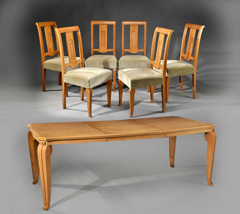 A rare dining room table in white leaded oak and a rectangular top with folded corners together with a set of six chairs in white leaded oak with carved ancient style characters and green velvet seats, circa 1940. The table is sold with an oak