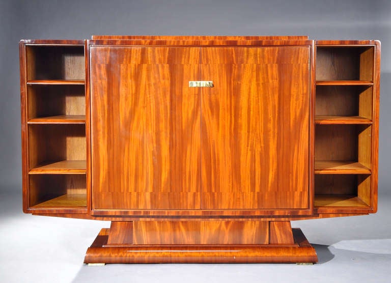 Bookcase in mahogany veneer opening by two doors onto drawers with three open shelves on each side.
Branded seal « Rousseau et Lardin ».
circa 1935.