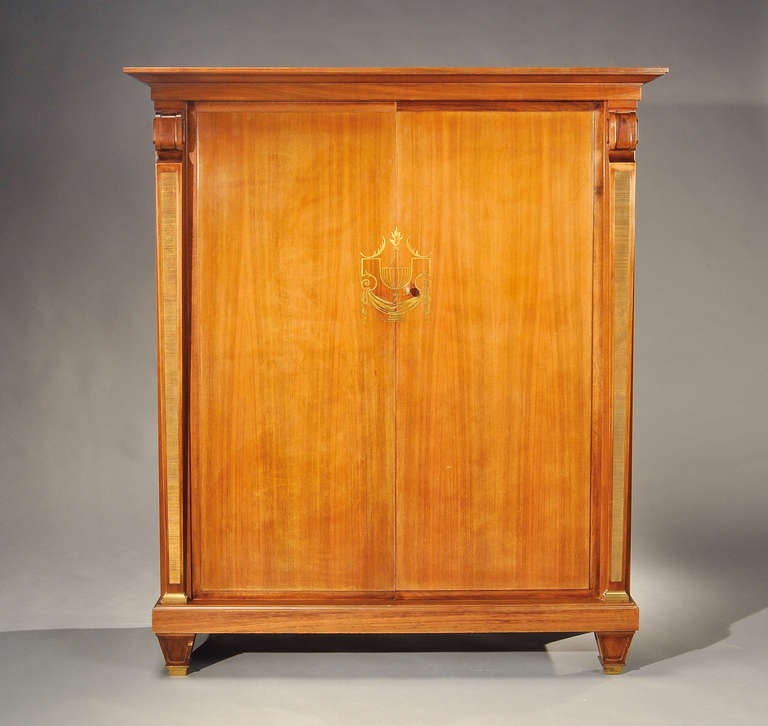 A mahogany veneer wardrobe with a central, incised decoration in gilded brass 
representing a Médicis vase and two doors opening onto sycamore veneer storage space flanked by two grooved metal pilasters.
Branded.
Circa 1940-1950.

