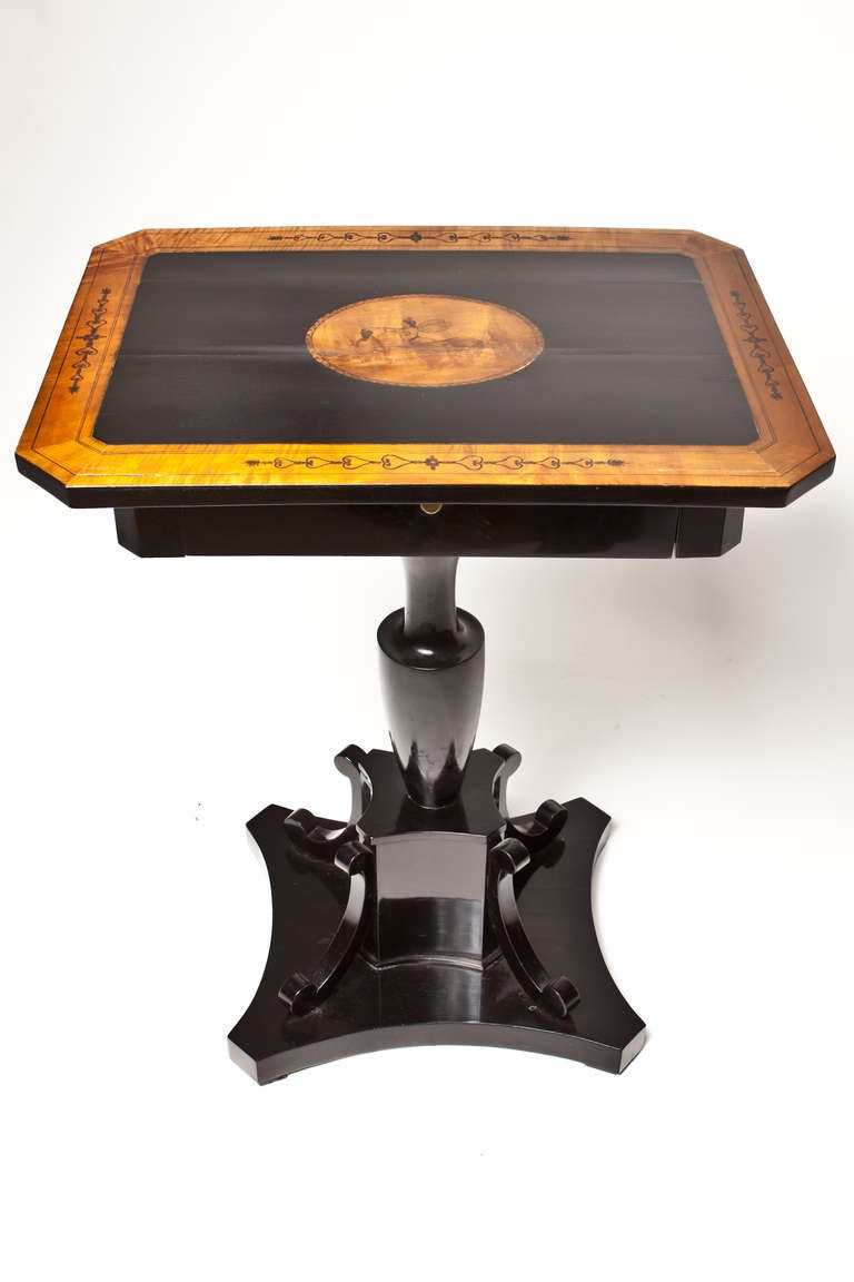 Continental burlwood and ebonized work table, rectangular top with  figural inlay, canted corners over single drawer, raised on an ebonized baluster standard with C-scroll brackets ending in a quadripartite base.