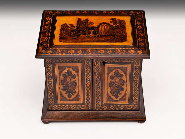 Tunbridge ware cabinet veneered in rosewood with a view of Muckross Abbey, has mosaic borders surrounding floral patterned doors and is the work of Henry Hollamby.

The doors open on this Tunbridge cabinet to reveal four graduated drawers with