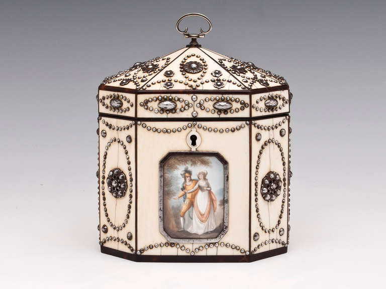 Very rare octagonal tea caddy with faceted cut steel decoration and tortoiseshell edging. Features a painted plaque of a sweet young courting couple behind cut steel framed glass. The top has a silver looped handle, the interior is faced in