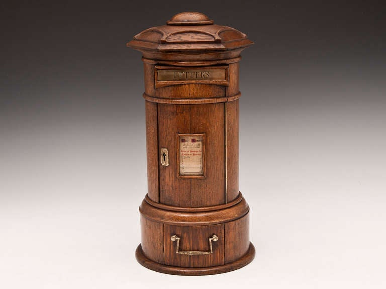 A lovely example of a miniature cylindrical post box with hexagon lobed dome carved top. The front has a brass letter plate and glass panel with collections times on the front of the lockable door.
The base has a drawer and brass swing-handle. We
