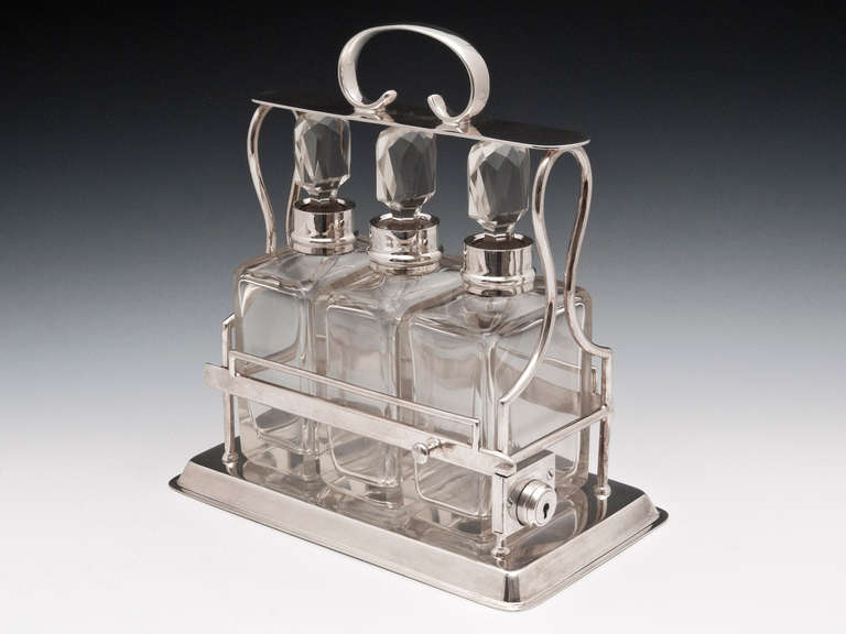 Silver plated tantalus by Birmingham silversmith Hukin & Heath with three decanters with sterling silver collars and cut glass stoppers.

Once unlocked the lock mechanism can be pressed allowing the side to be lifted up so the decanters can be