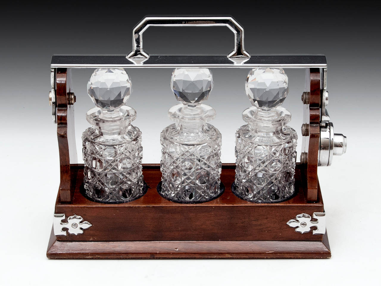 Miniature Betjemanns Walnut Tantalus. 
The miniature Tantalus has a silver plated carrying handle and decorative corners supports on all four sides. 

The Tantalus contains three superb round lead crystal hobnail cut glass decanters with faceted