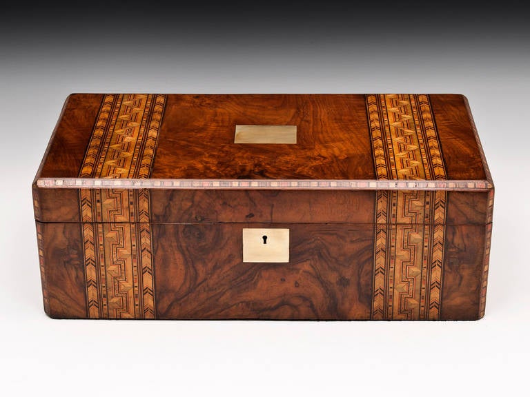 Writing box with inlaid mosaic designs running over the top with brass escutcheons. 

The interior features a red leather writing surface, removable pen tray and compartments for ink wells. The top and bottom of the writing surface can be lifted