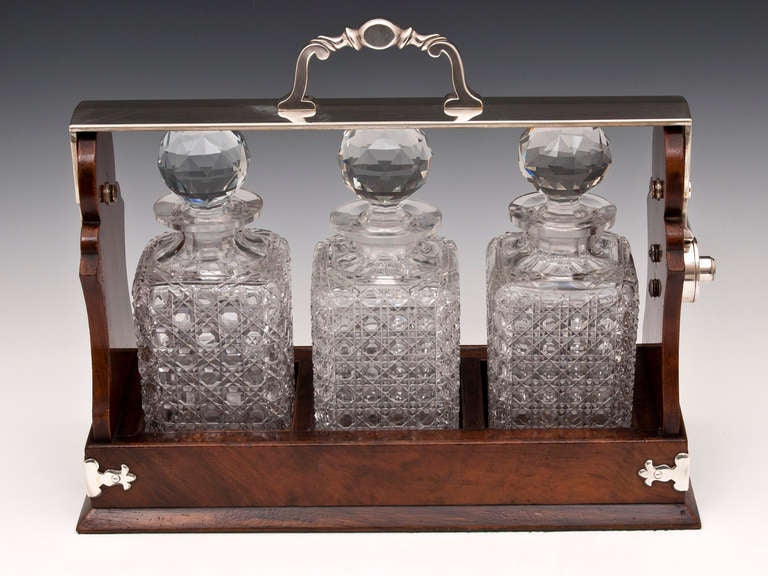 Walnut Betjeman Tantalus with three large hobnail cut crystal decanters. 

The tantalus lockable handle swings down to release the decanters. This is achieved by unlocking the handle and pressing the lock mechanism down. 

The walnut base has