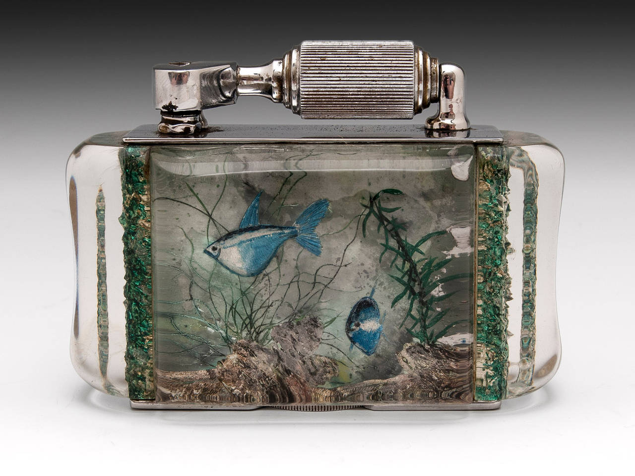 Aquarium table cigarette lighter by McMurdo. 
McMurdo was a former designer for Dunhill. 

This half-giant size lighter features reverse carved and painted Lucite panels with decoration of fish swimming underwater and features silver plate
