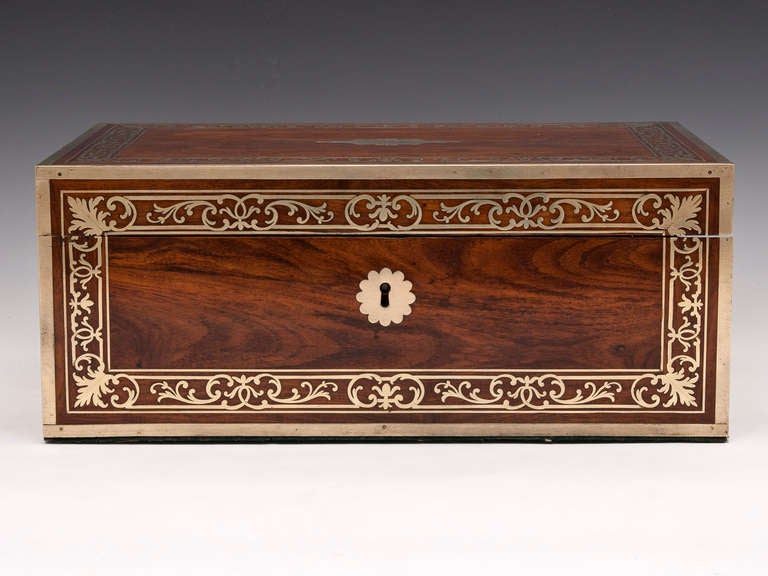 Kingwood writing box with inlaid floral brass n the front and top. Brass escutcheons and edging, and flush campaign carry handles on either side.

Inside features a gold tooled black leather writing surface, framed by brass stringing, a pen tray and