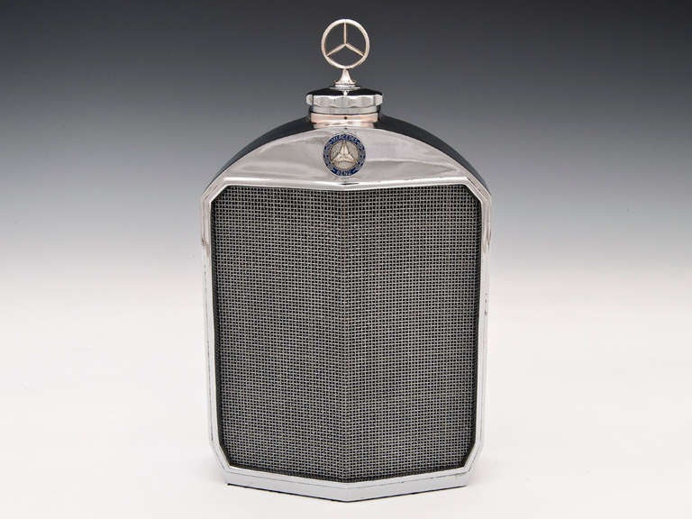 Mercedes Decanter with chrome radiator grill made by Classic Stable Ltd. 

The case is heavy chromium plated metal and surrounds a glass container. There is a slot in the casing at the rear allowing visibility of the contents with Baize cloth to