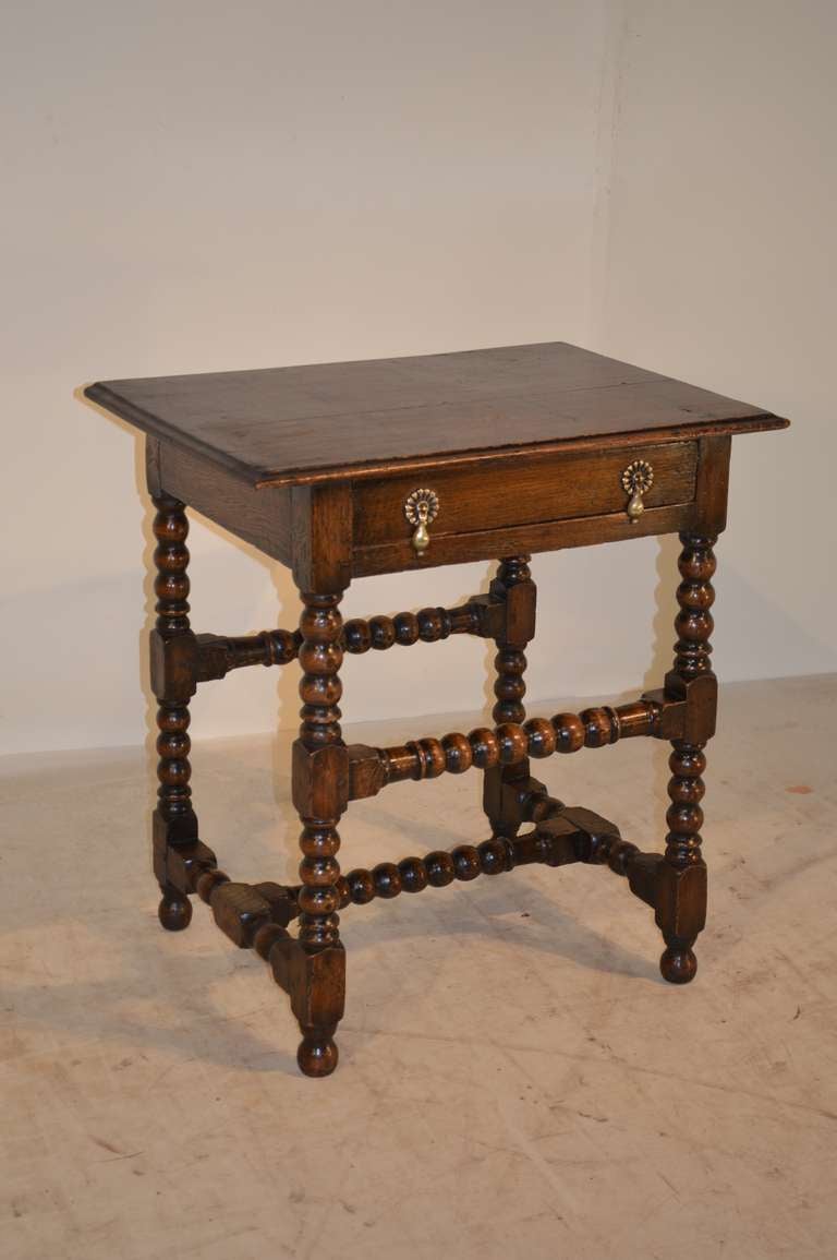 18th-C. English oak side table with a two plank top with a beveled edge, following down to a single drawer. The legs and stretchers are of a bobbin style, resting on bun feet.