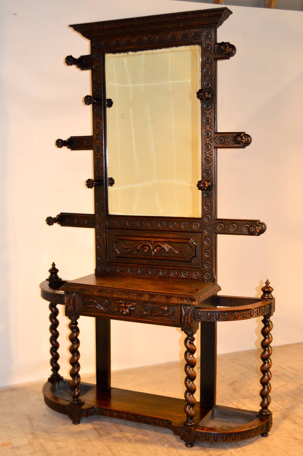 19th-C. English oak hall stand of exceptional quality. The top has a crown molding over a central framed mirror, flanked by turned and reeded hat and coat hooks, following down to a base with a central glove drawer, which is flanked by two cane and