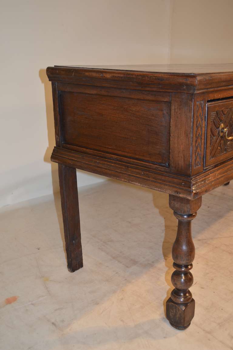 17th century English server made from oak. It has a plank top with a molded edge, following down to two drawers with exquisitely carved drawer fronts and paneled sides. Supported on front legs which are hand-turned and simple plank back legs, as was