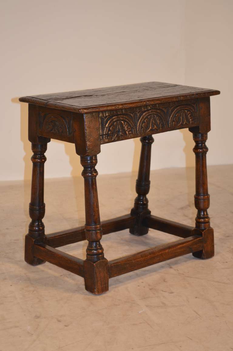 Late 17th-C. English oak joint stool with a beveled edge around the top, which has shrinkage.  The apron is carved with early decoration and follows down to lovely turned and splayed legs, connected by stretchers.