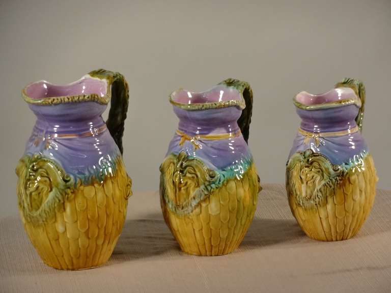 Joli ensemble de trois pichets en majolique à décor de têtes de bélier. Petit éclat à l'intérieur du bord d'un pichet. Le pichet moyen mesure 6 x 4,75 x 8,25 et le petit pichet mesure 5,5 x 4,25 x 7,5.
