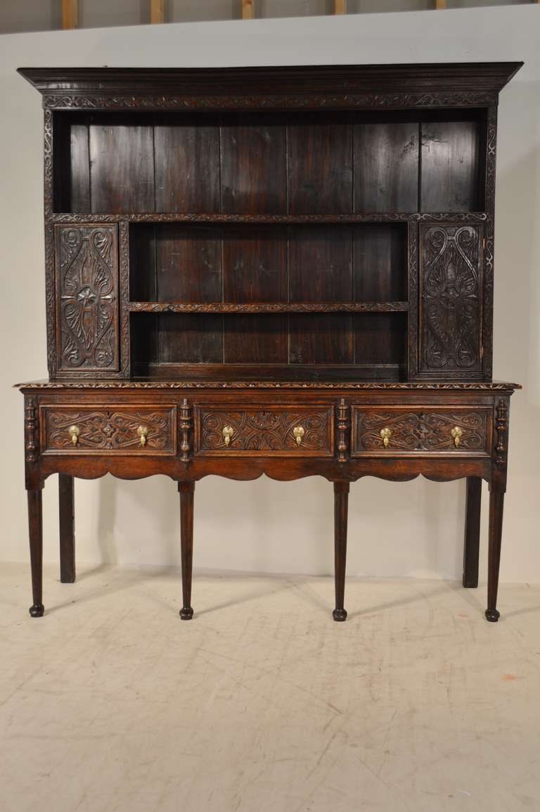 Early 18th century. Welsh dresser made from oak. Gorgeous hand-carved decoration on drawer fronts, front doors and framing the cabinet. Lovely scalloped apron. Resting on pad feet.