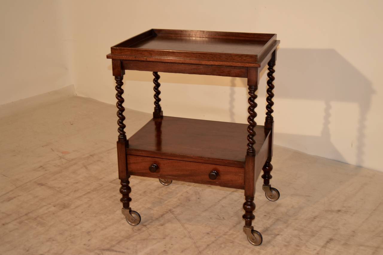 19th-C. English tea cart made from mahogany.  The top shelf has a wooden gallery on all four sides, surrounded by a nice molded edge.  The shelf supports are exquisitely hand turned barley twist and it has a lower shelf which contains a single