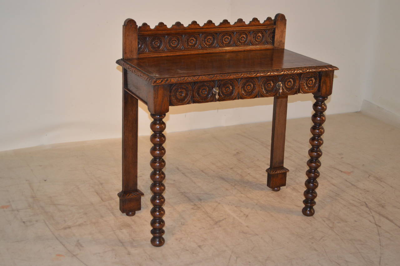 19th-C. English oak console table with carved and scalloped backsplash and a single drawer which has a carved decorated drawer front. The legs are flat in the back for placement against a wall and are finished with lovely block and bun feet.  The