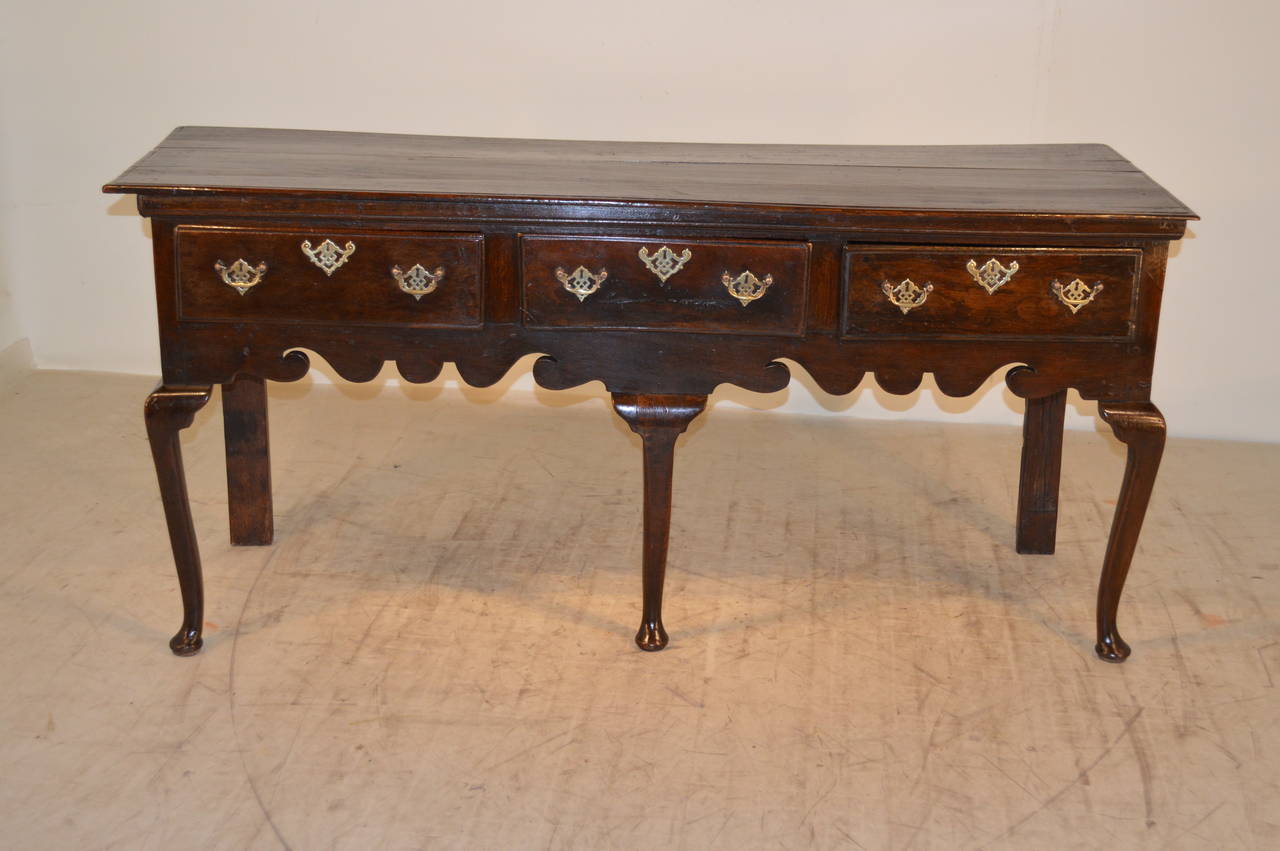 Early 18th century English oak sideboard with a two board plank top, which is beveled around the edge. The apron is wonderfully hand-scalloped on the front and sides and contains three drawers. The drawers have beveled edges as well.  There are