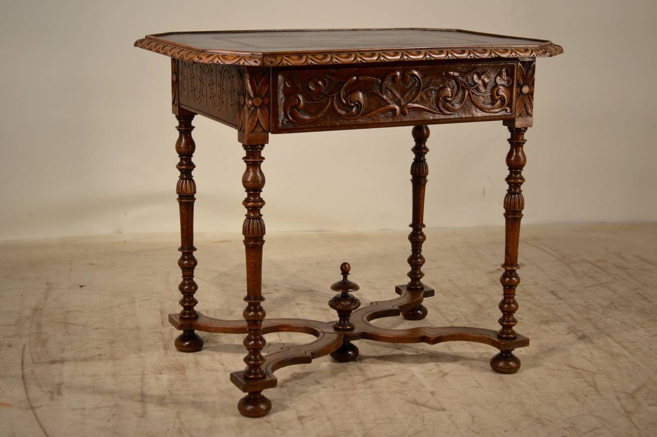 19th century. French walnut side table with a leather top.  The top has a beveled and gadrooned edge, following down to a wonderfully hand carved apron on all four sides, with the drawer front being carved the most relieved.  The legs are hand