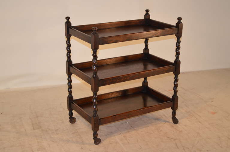 Late 19th-C. English oak tea cart with nicely turned barley twist shelf supports separating three shelves.  Raised on original casters.
