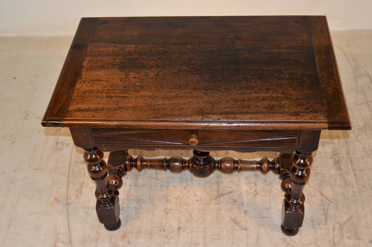 18th Century French side table made from walnut.  The top has banded ends and is beveled around the edge.  There is shrinkage in the top and some marking from age and use. There is a single drawer with routed decoration and a scalloped apron below. 