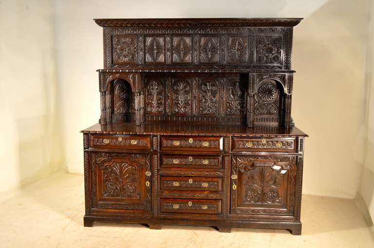 Welsh oak dresser, circa 1720. The top of the dresser is a flat back highly carved panel with carved crown molding at the top. It has a shelf which is supported on hand-carved arches with reeded columns. The base has four central drawers, flanked by