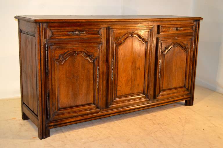 18th century French enfilade made from oak.  It has a plank top with banded edges, following down to a wonderfully raised paneled case with a central carved paneled door flanked by two paneled  drawers over two carved paneled doors. They each open