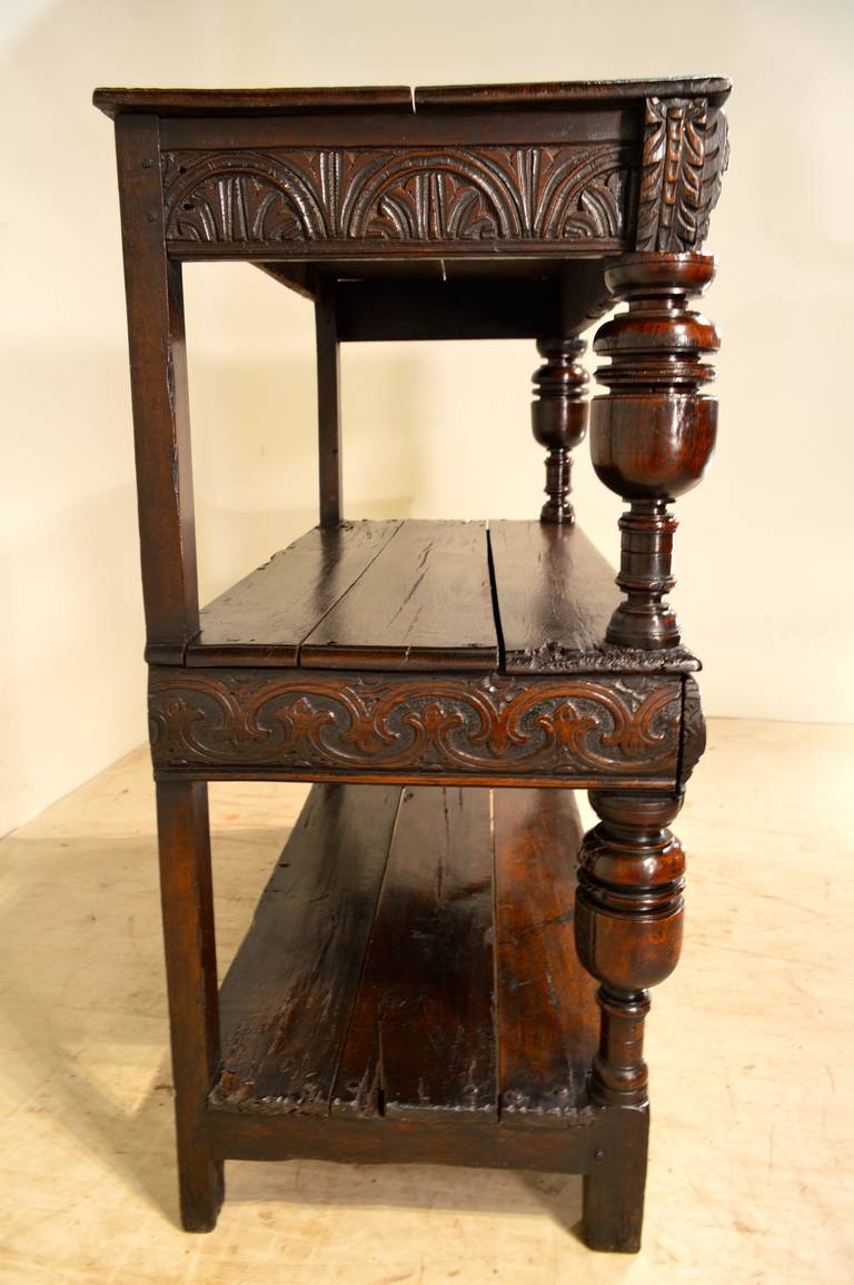 16th century period Elizabethan oak court cupboard from England. The top and shelves are made from planks, which have bevelled edges and pegged construction, following down to hand-carved aprons, the centre one is a drawer. The shelves are joined by