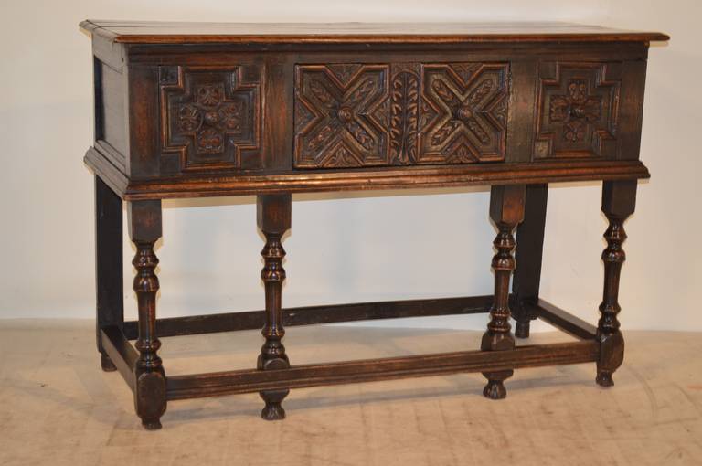 17th century English oak server with a two plank top which has a beveled edge and rose head nail and pegged construction. The case has paneled sides and the front has two false drawers flanking a central drawer, all with geometric and carved
