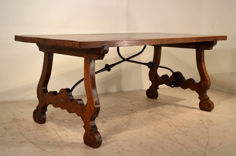 Early 20th century Spanish dining table made from oak. The top is made up of four thick planks and has elegantly scalloped legs and stretchers supported on scrolled feet and joined by iron support brackets.