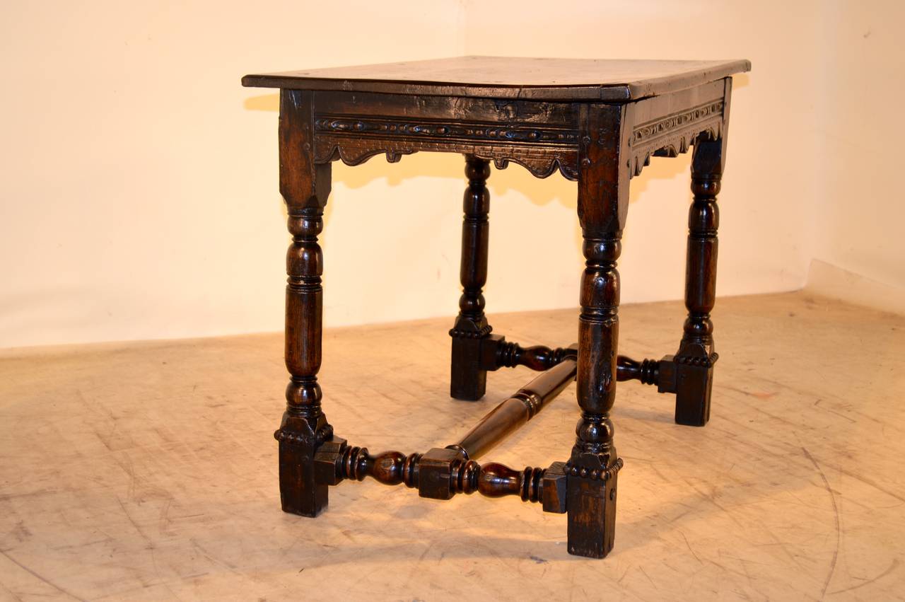 English oak plank-top table with pegged construction, following down to a carved decorated and scalloped apron and early turned legs, joined by a cross stretcher. Beaded around feet.