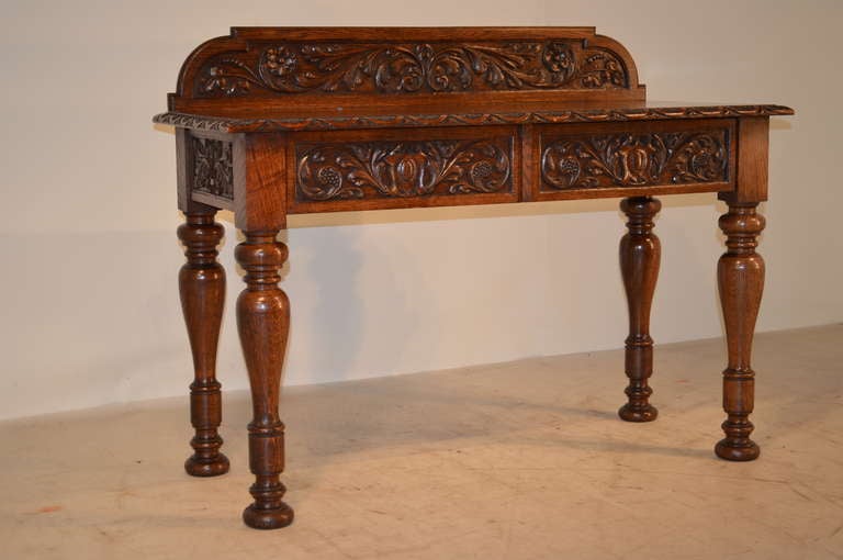 19th-century English oak hall table with carved backsplash following down to the top which is gorgeously figured and has a beveled and gadrooned edge. Apron has two drawers with carved drawer fronts. Legs are wonderfully hand-turned and are resting