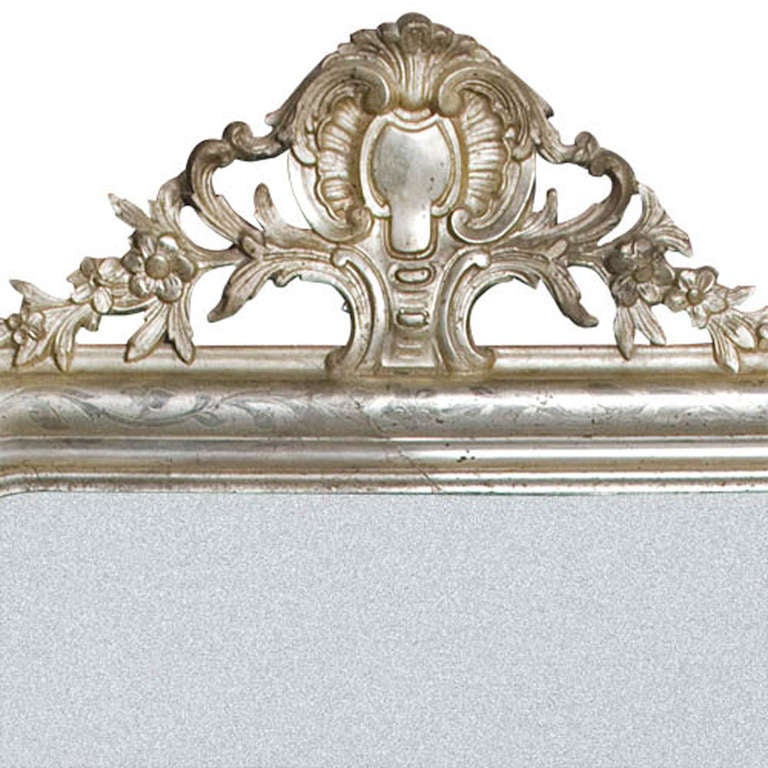 This beautiful French Louis Philippe mirror has an elegant crest on top. Though the mirror is silver gilt, this originally was a gold mirror. The silver gilding is authentic and its metallic shine was the base for a different shade of gold. The