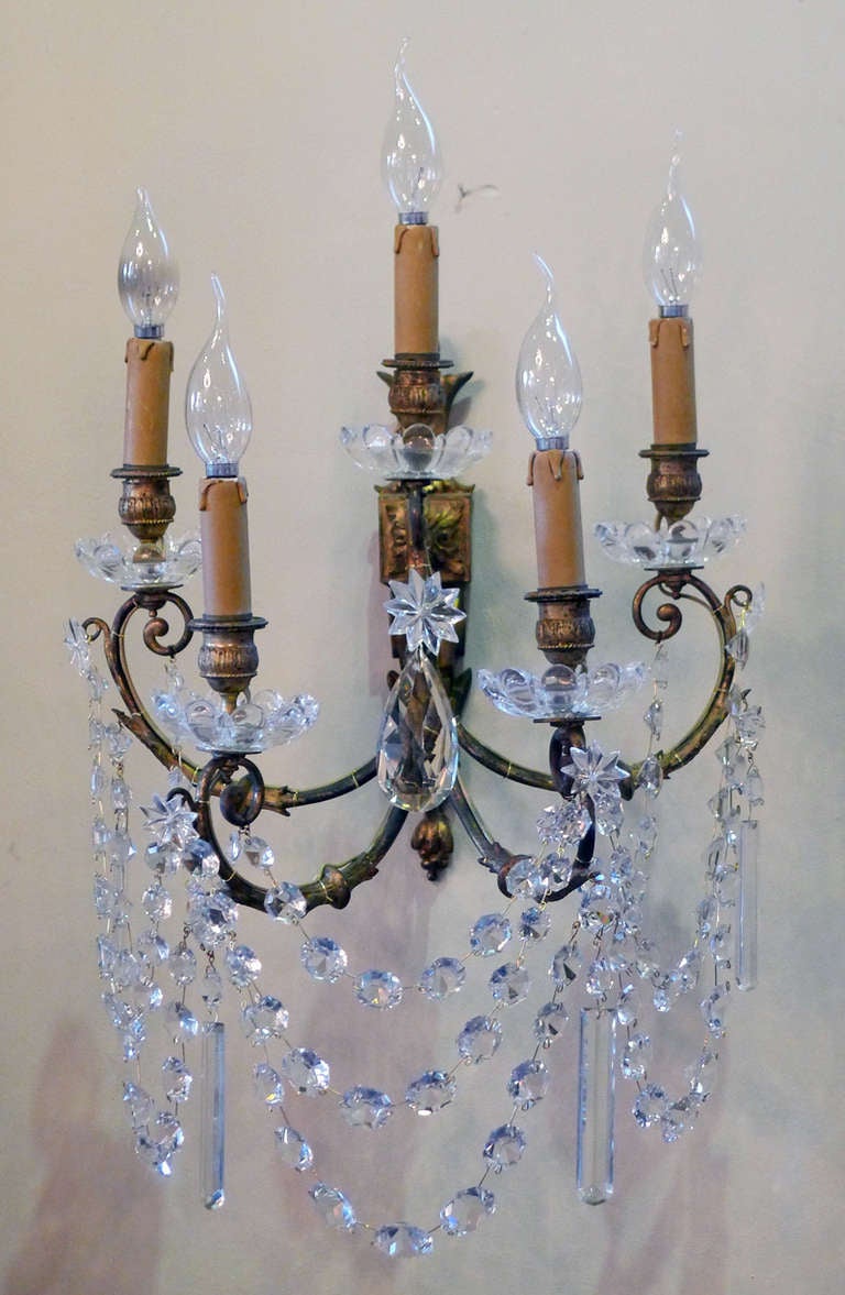 Pair of French wall sconces hung with crystal. 
This frame is fire gilded and each sconce has five lights.
Beautiful pair, in perfect condition.
The oval crystal in the middle is 9 cm long; the rectangular crystals are 10 cm long.