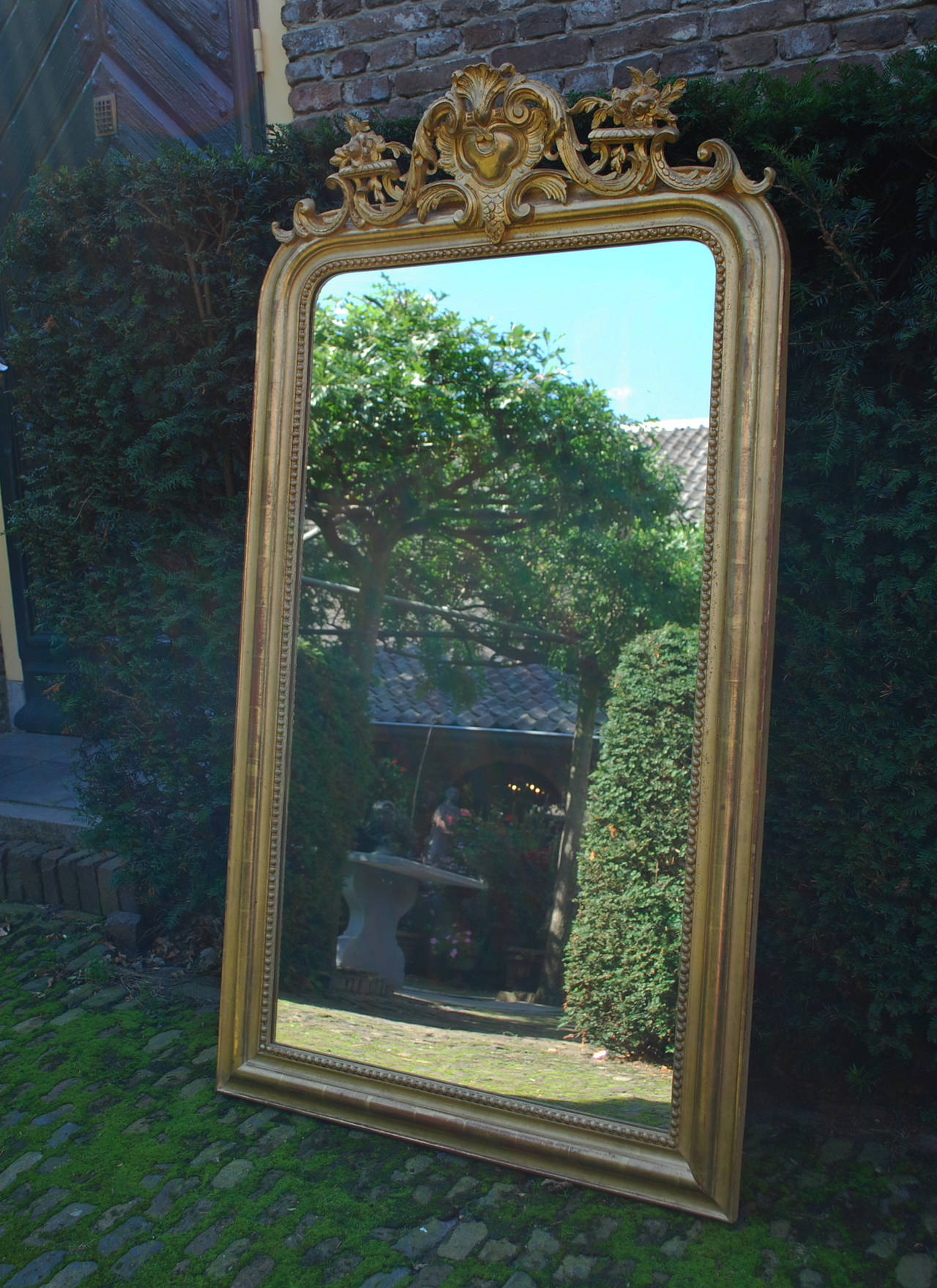 This beautiful antique French mirror with rounded uppers corner and ornate crest has a very strong gold color. Its golden appearance has slight variations in color. The most elevated parts on the frame as well as the crest are made in polished gold