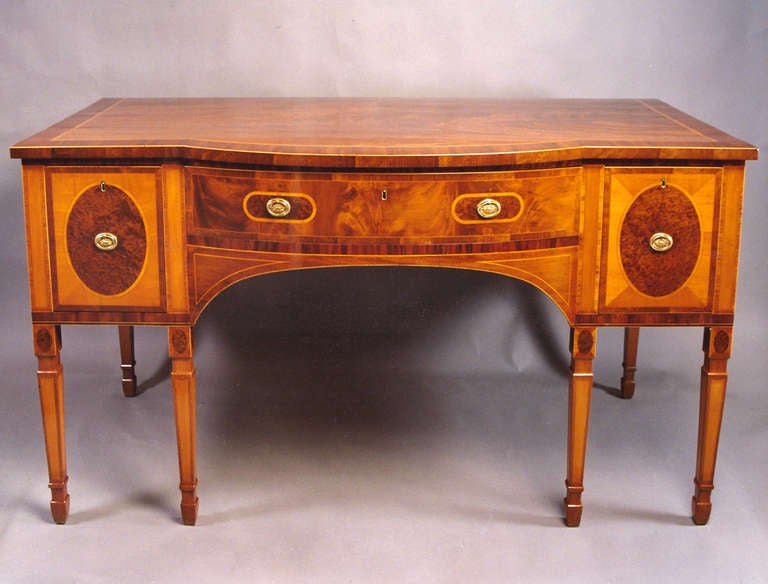 An early George III period mahogany sideboard of rectangular form with bowed centre, comprising three drawers over six square taper and moulded legs or large proportions. Veneered and inlaid with burr maple, purpleheart, goncalo alvez and satinwood