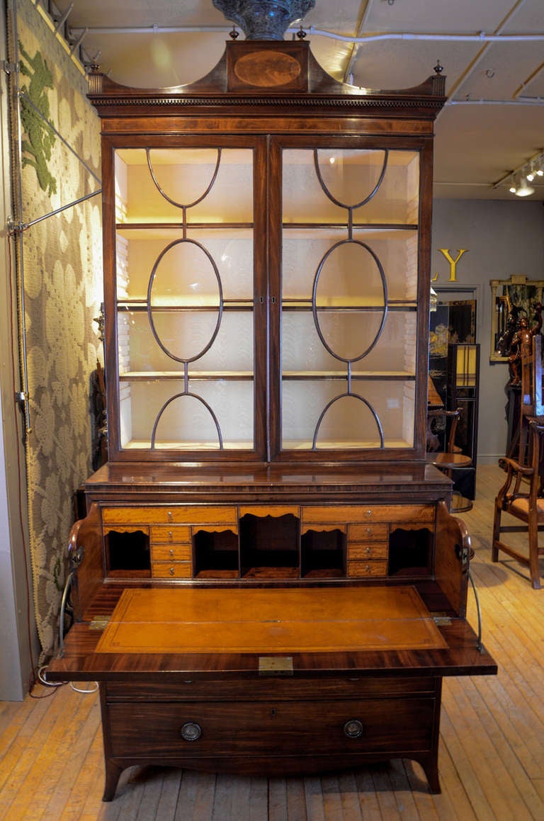 An important George III Secretaire Bookcase to designs by Thomas Sheraton, stamped on the three lower drawer linings by the maker, Lovell of Chichester.
The upper part with swag shaped top cornice with central oval inlay of satinwood and six finials