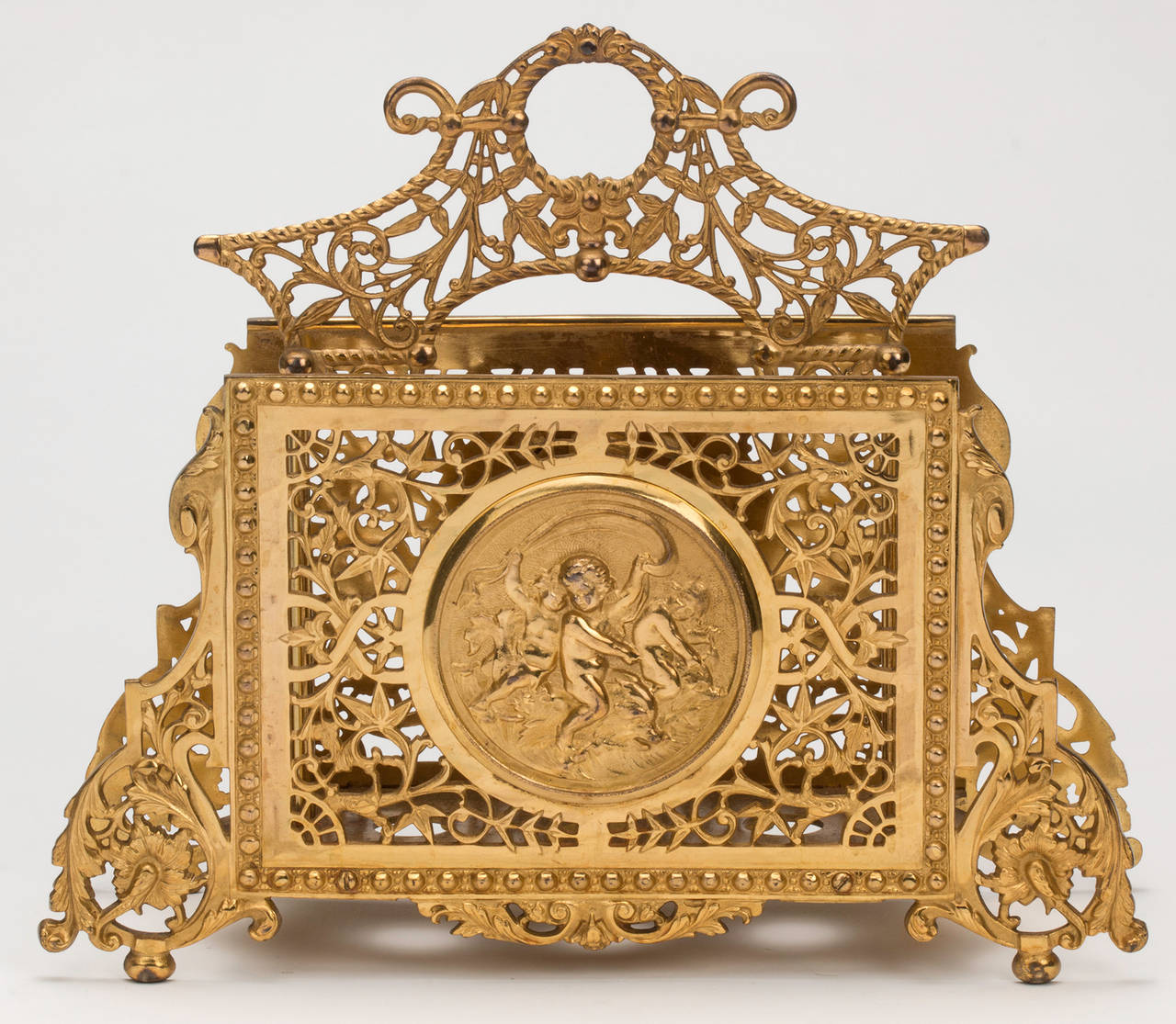 Beautiful and functional gilt bronze  magazine rack. Decoratively elaborate pierced work around cherub medallion.