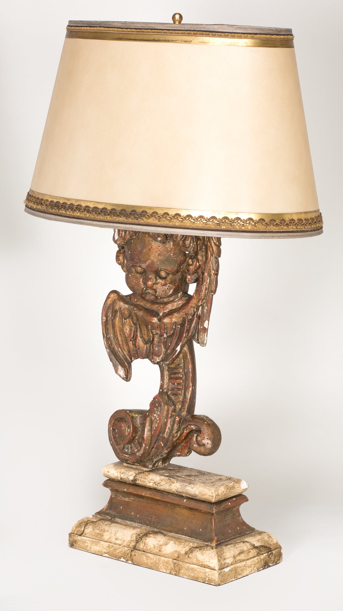 Pair of lamps carved giltwood of cherub elements, circa 1860s. Plinth stand is painted faux marble. Handmade parchment gilt trim shade. 13 D x 19 W x 11 H. Lamp without shade dimensions are shown below.