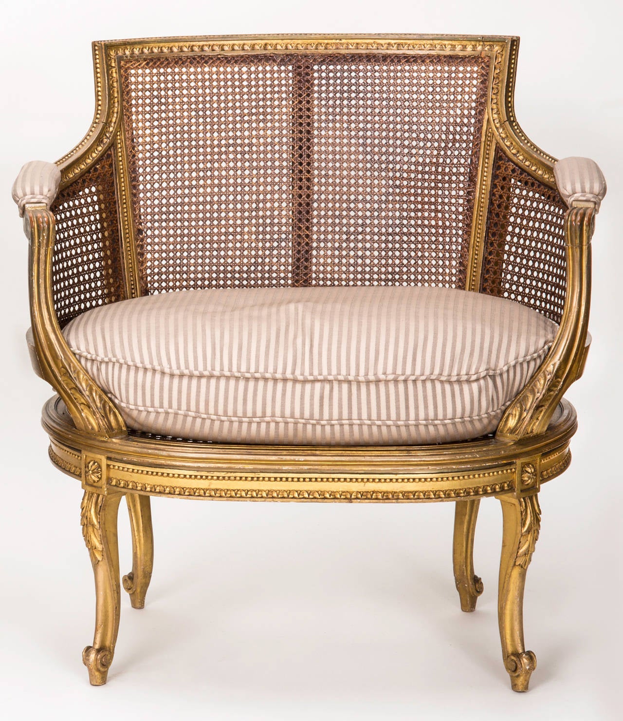 Pair of wonderful French armchairs with cane seat and back, circa 1900s.  Beautifully carved giltwood frame with graceful cabriole legs. Amply sized comfortable seating. Loose down seat cushions in stripe linen. The caning and chair frames are in